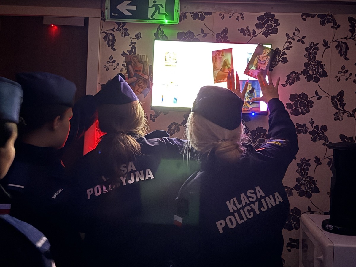 Wnętrze przyczepy edukacyjnej Uczniowie klasy policyjnej wewnątrz symulowanego pokoju ze zdjęciami ofiar handlu ludźmi