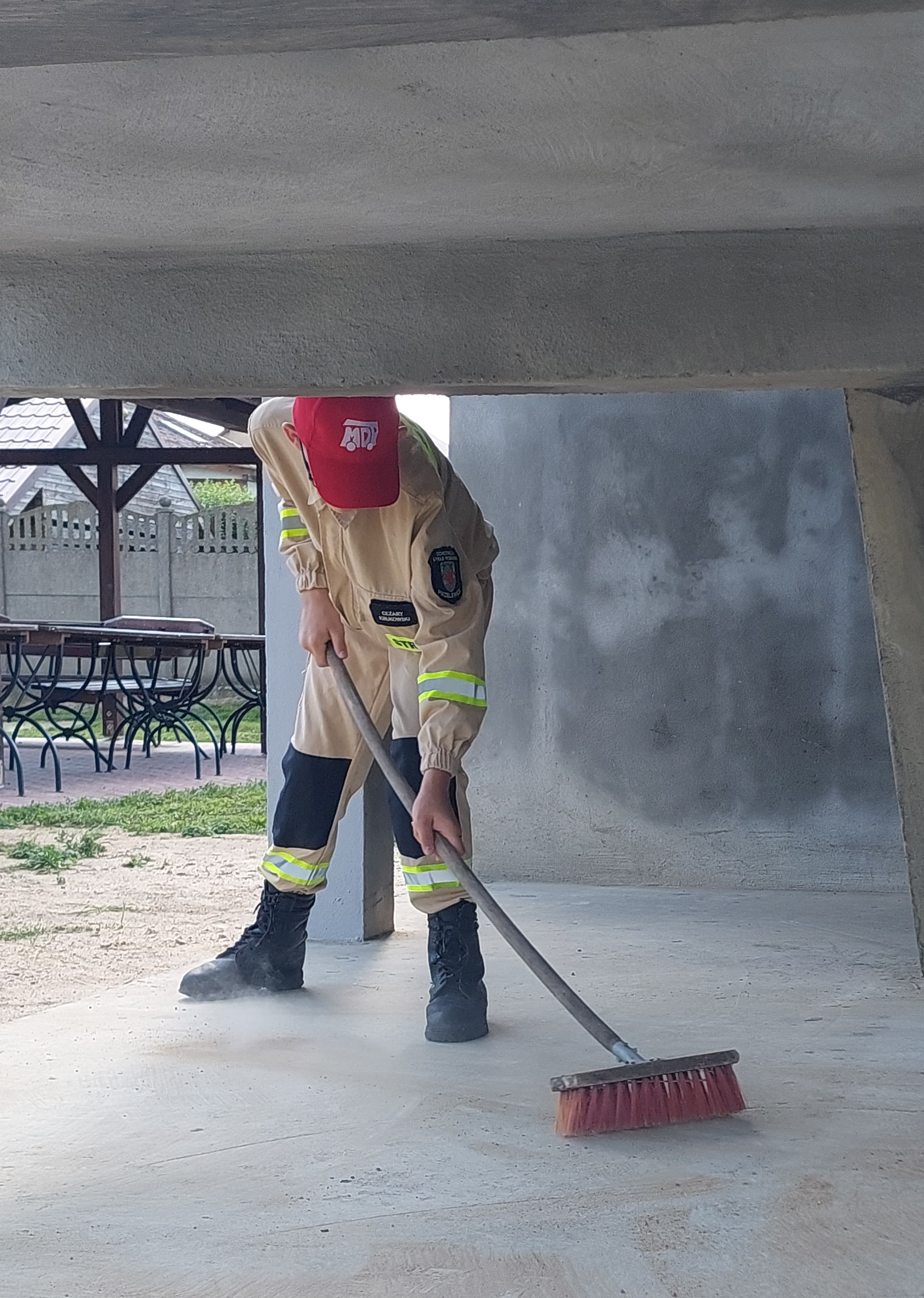 Członek Młodzieżowej Drużyny Pożarniczej zamiata wieżę strażacką. ....a po zajęciach trzeba posprzątać.