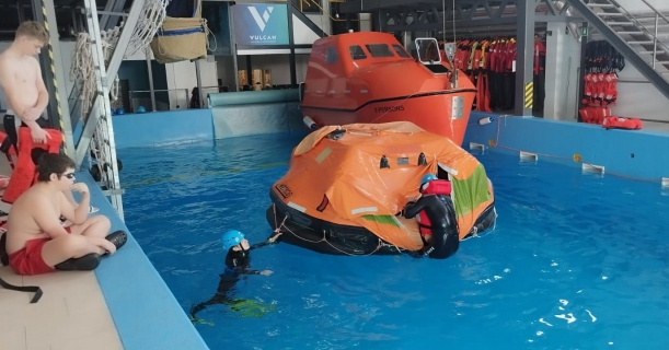 Widok na basen treningowy z unoszącą się na wodzie pneumatyczną tratwą ratunkową.