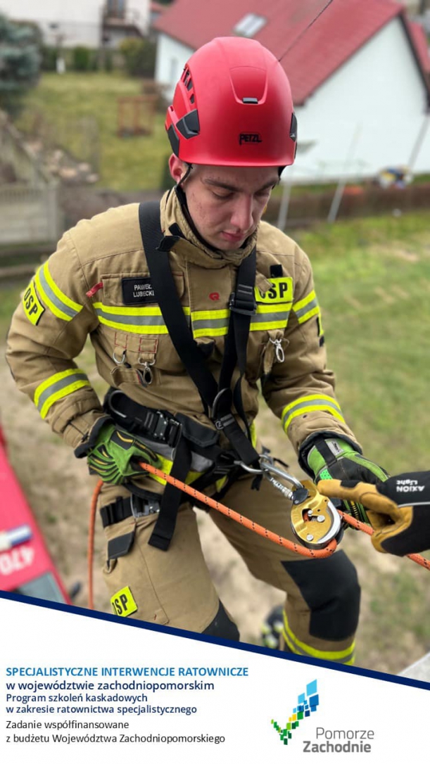 Plakat informujący o szkoleniu Ratownik OSP w uprzęży wspinaczkowej, gotowy do zjazdu z wieży do ćwiczeń strażackich,