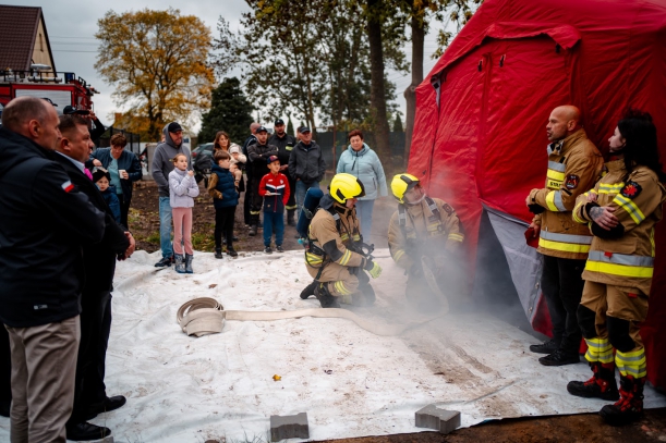 Strażacy w aparatach oddechowych szykują się od wejścia do namiotu - komory dymowej