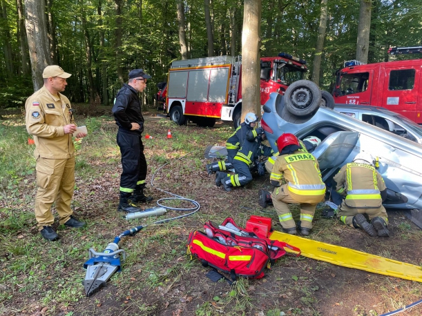 Przewrócony na dach samochód, z którego pięciu strażaków próbuje wydostać poszkodowanych
