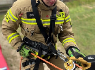 Ratownik OSP w uprzęży wspinaczkowej, gotowy do zjazdu z wieży do ćwiczeń strażackich, 