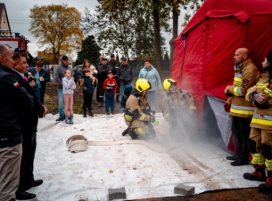 Strażacy w aparatach oddechowych szykują się od wejścia do namiotu - komory dymowej