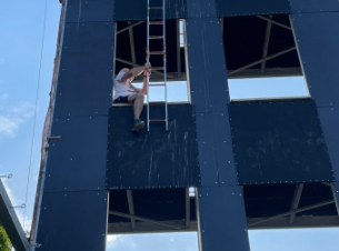 Instruktor z parapetu pierwszego piętra wieży strażackiej wysuwa drabinę, aby zaczepić ją o parapet drugiego piętra.